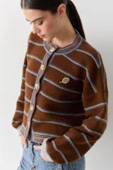 Cardigan de lana color bordó con cuello redondo, cierre frontal de botones y mangas largas. Presenta detalles de ribetes en contraste en cuello, puños y borde inferior, además de un bordado de raqueta de tenis en el pecho.