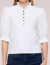 Buzo de algodón blanco con cuello mao y volados, manga tres cuartos abullonada y botones metálicos decorativos en la parte frontal.