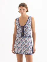 Chaleco de punto semiliviano con diseño jacquard en tonos blanco, azul y rojo, escote en V profundo y cierre frontal con tiras para anudar.