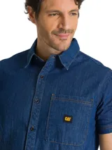 Camisa de jean de manga corta, color azul, con cierre frontal de botones, cuello camisero y bolsillo en el pecho con etiqueta de la marca.