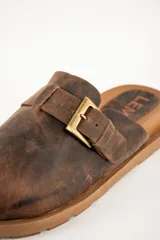 Zueco marrón de cuero con hebilla lateral y suela de goma.