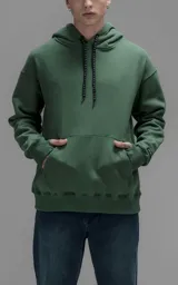 Hoodie oversize color verde, confeccionado en frisa premium con textura gamuzada. Presenta capucha ajustable con cordones personalizados, bolsillo frontal tipo canguro y puños con abertura para pulgar.