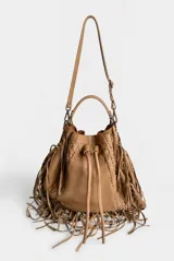Cartera estilo saco de cuero vacuno marrón, con flecos colgantes, asa tubular rígida y detalles de costuras decorativas. Cuenta con cordón ajustable en la parte superior adornado con borlas y herrajes metálicos.