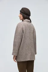 Chaquetón de lana fina sin teñir, con cuello camisero, cierre frontal de botones y bolsillos delanteros. Diseño de corte recto y estructura clásica.