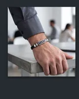 Pulsera masculina con banda de caucho negro y eslabones centrales de acero inoxidable con diseño geométrico grabado.
