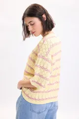 Sweater de punto fantasía color amarillo con líneas horizontales onduladas en color fucsia, de cuello redondo y manga corta.