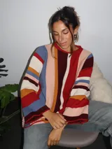 Sweater tejido a mano con terminaciones en crochet, de silueta oversize y mangas acampanadas. Presenta un diseño de rayas verticales multicolores en tonos tierra, rojo, azul y crema.