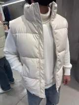 Chaleco puffer de cuero sintético en color beige, con diseño acolchado, cuello alto y cierre frontal completo.