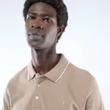 Remera polo de piqué de algodón color beige, con cuello y puños con ribete blanco, cierre frontal con botones y pequeño logo bordado en el pecho.