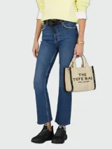 Bolso tipo tote Marc Jacobs modelo The Small Tote, color beige con detalles y texto en negro que dice "THE TOTE BAG MARC JACOBS". Cuenta con asas superiores y laterales para llevar en la mano o al hombro.