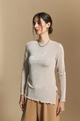 Top de manga larga con textura suave y leve brillo. Presenta una silueta al cuerpo, tajos laterales y terminaciones onduladas en el ruedo.