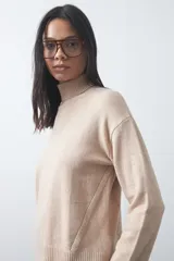 Polera de tejido liviano color negro con cuello alto y silueta relajada. Presenta mangas largas con puños ajustados y recortes laterales que aportan estructura al diseño.