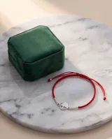 Pulsera de hilo rojo con técnica de macramé, que presenta un dije central circular con diseño calado de árbol de la vida en plata y pequeñas esferas plateadas decorativas a ambos lados.