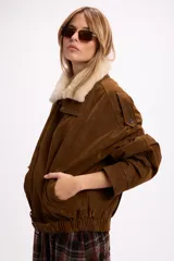 Campera de gamuza negra con cuello de piel sintética en color crema, cierre frontal, corte oversize y diseño estructurado con hombreras.