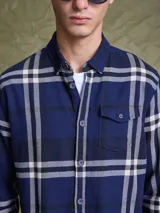 Camisa de manga larga en color azul noche con un patrón de cuadros finos en tonos rojos y verdes. Presenta cuello clásico, cierre frontal con botones y un bolsillo en el pecho con solapa.