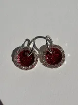 Aros colgantes con forma circular, hechos de resina color lila y borde de strass plateado. El aro es de acero quirúrgico plateado.