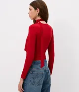 Blusa entallada de microfibra color blanco, con escote en V, mangas largas y detalle de frunces en los laterales. Presenta un lazo integrado en el cuello que permite anudarlo, aportando un toque sofisticado al diseño.