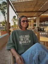 Remera gris con efecto acid wash y diseño oversize. Presenta un estampado frontal con la inscripción "KILLING IN THE NAME OF" y la frase "NOW YOU DO WHAT THEY TOLD YA".