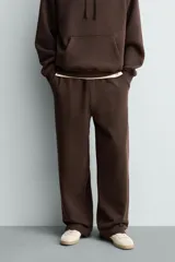 Pantalón jogger de corte relajado y pernera ancha, confeccionado en tejido de algodón con interior perchado. Presenta cintura elástica con cordón interior, bolsillos laterales y un bolsillo trasero de plastrón.