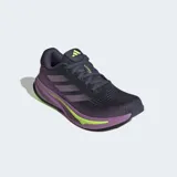 Championes de running Adidas Supernova Rise para mujer, con capellada de malla en tonos gris oscuro y morado, tres franjas moradas y detalles en amarillo neón. La mediasuela es gruesa, predominantemente morada con una capa de amortiguación en amarillo neón que lleva la inscripción "DREAMSTRIKE+".