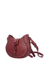 Cartera tipo bandolera de ecocuero color bordó, con diseño semicircular y detalle de tachas metálicas plateadas en el frente. Cuenta con una solapa central con cierre magnético y argollas decorativas, además de una correa ajustable para llevar al hombro o cruzada.