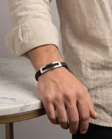 Pulsera de diseño masculino compuesta por una banda de cuerina trenzada en color negro y una placa central rectangular de acero inoxidable con acabado pulido.