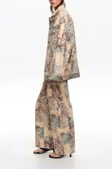 Chaqueta larga de corte oversize confeccionada en algodón con estampado patchwork en tonos beige, verde y marrón. Cuenta con cierre frontal con botones, cuello camisero, mangas largas, bolsillos con solapa en el pecho y bolsillos laterales.