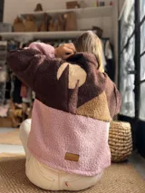 Buzo de tejido tipo corderito con diseño de bloques de color en tonos marrón, chocolate y rosa. Presenta un aplique decorativo en la espalda con forma de paisaje montañoso y etiqueta de marca en el ruedo.