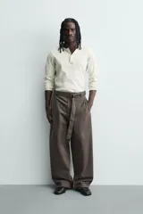 Pantalón de corte wide fit confeccionado en tejido con algodón. Presenta pliegues frontales, cintura ajustable con cinturón integrado, bolsillos laterales y bolsillos traseros de vivo. Cierre frontal con cremallera y botón.