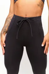 Calza deportiva negra de tiro alto, confeccionada en poliamida con elastano, con costuras laterales visibles y cordón ajustable en la cintura.