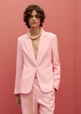 Chaqueta de lino color rosado, con diseño recto, cuello con solapas de muesca y cierre frontal de un botón. Cuenta con mangas largas con puños abotonados, dos bolsillos de ribete delanteros y abertura posterior en el bajo.