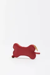 Monedero pequeño de cuero reconstituido color rojo brillante, con forma de hueso de perro. Posee cierre de cremallera dorado y una correa corta de cuero para sujetar.