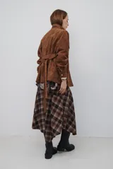 Chaqueta de gamuza en tono marrón oscuro, con cuello alto, cierre frontal con cremallera y botones a presión, bolsillos frontales con solapa y cinturón ajustable en la cintura.