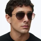 Lentes de sol estilo aviador con montura metálica fina en color dorado y lentes degradadas en tono marrón. Presentan un diseño ligero con puente doble y terminales de patillas en acetato.