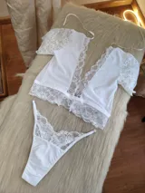 Conjunto de lencería blanco compuesto por un top de encaje con mangas cortas y una bombacha tipo colaless con detalles de encaje.