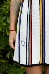 Vestido corto blanco con rayas verticales en azul, amarillo y marrón. Tiene escote redondo, breteles anchos y corte holgado.