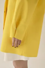 Cazadora impermeable de acabado engomado en color amarillo, con capucha ajustable, cierre frontal con botones a presión, bolsillos laterales y mangas largas ajustables.
