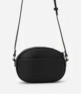 Cartera tipo camera bag pequeña, color marrón camel, de forma ovalada con superficie texturizada. Cuenta con correa ajustable larga, cierre principal con cremallera dorada y un pequeño bolsillo frontal con cremallera.