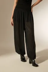 Pantalón tipo babucha de color negro, confeccionado en tela semitransparente con textura de rayas verticales y pequeños detalles en relieve. Presenta una cintura elástica cómoda y un corte holgado que se ajusta ligeramente en los tobillos.