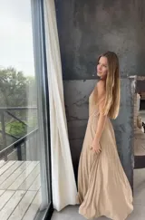 Vestido largo de un solo hombro, confeccionado en tela plisada con acabado brillante. Presenta un diseño entallado en la cintura con una falda fluida que incluye una abertura lateral pronunciada.