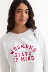 Remera de manga larga color beige con cuello redondo a la base. Presenta un estampado frontal con un dibujo de labios en color fucsia y la palabra 'BESITO' en color negro.