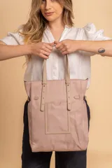 Bolso tipo tote bag de símil cuero color rosa pálido, con asas dobles y detalles de costura en color beige claro. Presenta un bolsillo frontal rectangular aplicado y herrajes metálicos.
