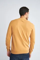 Sweater de punto color mostaza con cuello redondo y mangas largas. Presenta un estampado de pequeños motivos repetidos en contraste y un logo bordado en el pecho.