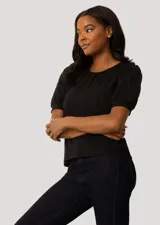 Blusa negra de corte recto con cuello redondo y mangas cortas abullonadas que presentan detalles calados con bordados en los hombros.