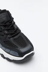 Zapatilla deportiva de estilo trekking con diseño técnico y urbano. Presenta una estructura combinada de paneles de malla y piezas de poliuretano, con sistema de cordones integrado y suela robusta con relieve para mayor estabilidad.