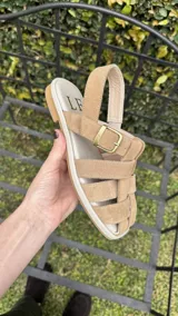 Sandalias de cuero negro con diseño de tiras entrelazadas, estilo huarache, con pulsera ajustable al tobillo mediante hebilla metálica.