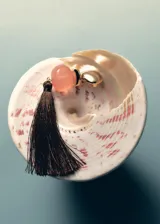 Aros largos compuestos por una pieza metálica dorada, una cuenta esférica de resina rosa y una borla colgante de hilo marrón oscuro.