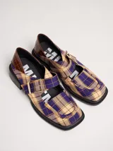 Zapatos tipo guillermina con punta cuadrada, confeccionados en lona resistente con estampado de cuadros escoceses en tonos beige, rojo y negro. Presentan una correa ajustable con hebilla metálica color bronce y una suela con taco de 4 cm.