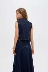 Chaleco de denim azul oscuro con bolsillos con solapa en el pecho, cierres decorativos y cierre frontal con botones metálicos.