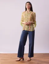 Blusa de gasa estampada con flores amarillas y verdes, marca Alex & Lili. Tiene cuello mao, mangas 3/4 acampanadas y cierre frontal con botones. Presenta volados verticales color naranja en el frente y en las mangas.